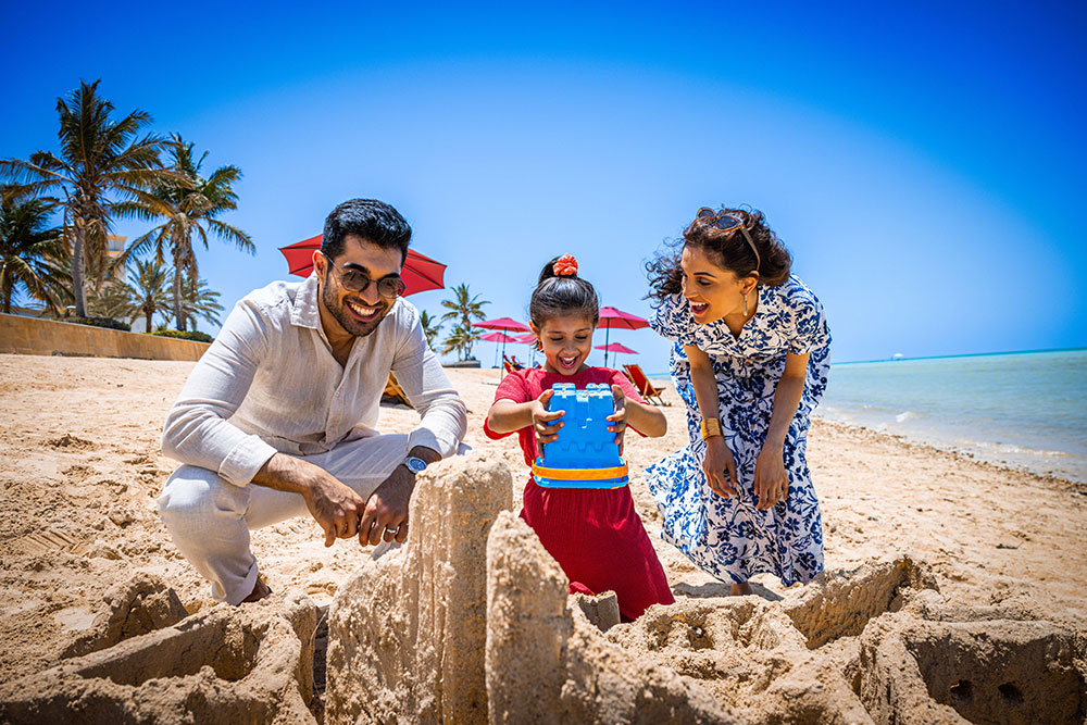 Child playing in the sand at the red sea with her parents