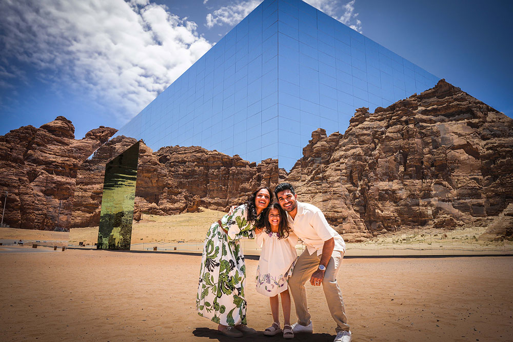 Family standing in front of mirror building in the desert in Saudi Arabia